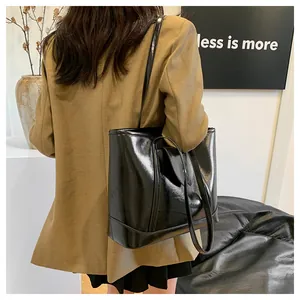 Close-up of a black glossy tote bag with dual long handles worn by a model on shoulder
