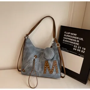 Macro detail of soft leather tote bag with M patch, rivets and a mini coin purse charm