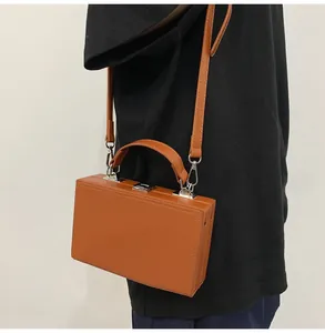 Close-up of brown hard-shell box bag with silver metal lock and detachable shoulder strap