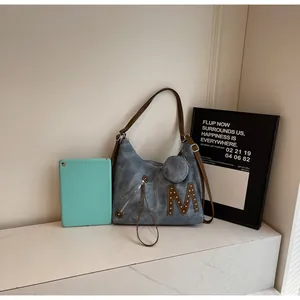 Detail of blue denim tote bag with metallic rivet M logo and brown leather straps