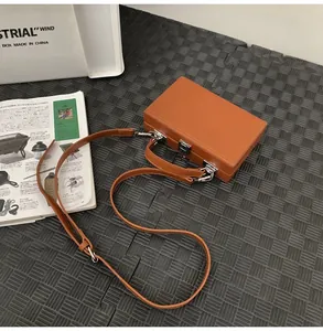 Detailed view of the brown hardshell box bag on a textured mat with a magazine