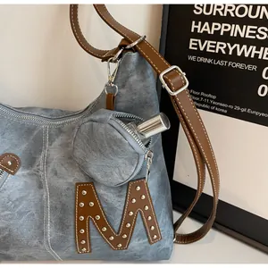 Close-up of denim tote bag featuring leather M patch with rivets and mini coin purse