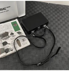 Close-up of black leather hard-shell box bag with metal latch and adjustable strap