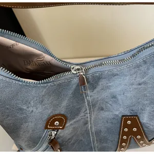 Detail of blue denim shoulder bag featuring silver zippers, rivets and leather accents