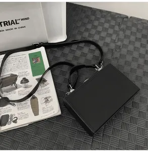 Detail of minimalist black hard shell crossbody box bag with textured leather surface