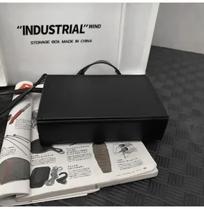 Detail of a minimalist black box bag on a magazine showing the rigid structure and handle