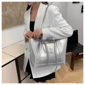 Model wearing a large silver metallic tote bag with glossy finish and shoulder strap
