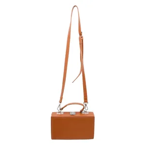 Macro view of bright orange hardshell box bag with silver metal clasp and matte finish