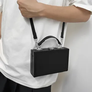 Minimalist black hard shell box bag with silver lock and detachable strap on white t-shirt