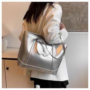 Silver metallic tote bag with wave-edge flap shown on shoulder in stylish indoor setting