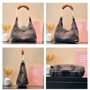 Detail view of large dark grey denim hobo bag showing its leather strap and crescent shape