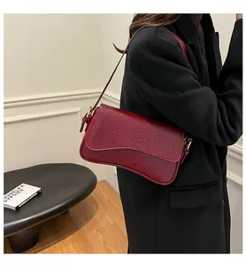 Détail du sac sous le bras en cuir bordeaux à motif lézard et boucle dorée élégante