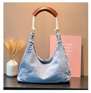 Detail of blue denim hobo bag with woven rope handle and brown leather shoulder guard