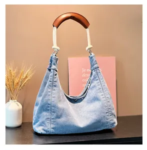 Detail of denim hobo bag with unique white rope strap and brown leather shoulder pad