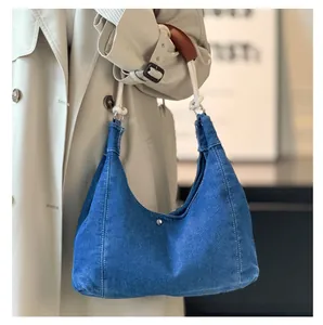 Detail of denim hobo bag featuring silver rivets and white rope shoulder strap on model