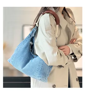 Detail of blue denim tote bag with white rope handles and brown leather shoulder pads