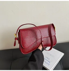 Détail du sac sous le bras en similicuir bordeaux à motif crocodile et boucle dorée