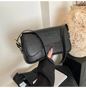 Détail du sac bandoulière noir avec texture motif lézard et boucles métalliques dorées