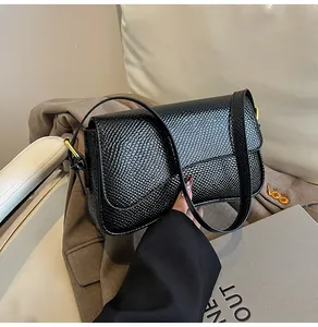 Détail du sac à bandoulière noir embossé lézard avec finition brillante et anneaux dorés