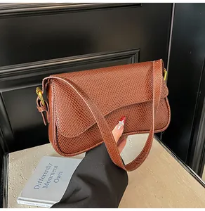 Détail du cuir gaufré marron foncé et boucle en métal doré sur un sac à bandoulière