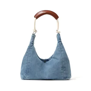 Blue denim crescent hobo bag with rope handle and leather grip on white background