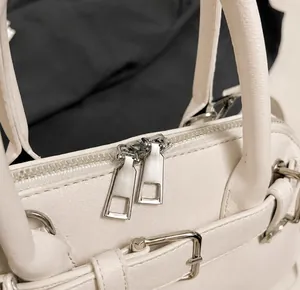 Close-up of white leather shell bag showing double metal zippers and stitching