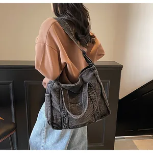 Detail of black denim tote bag with thick handles and adjustable strap on a model