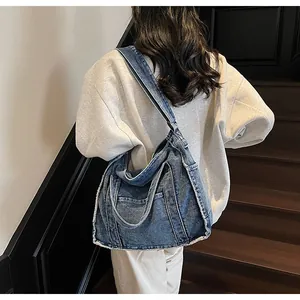 Detail of blue denim tote bag with frayed edges and utility pockets on a model