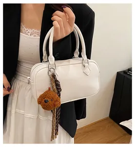 Close-up of white lychee leather Boston bag with teddy bear charm on model
