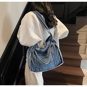 Blue denim tote bag with frayed edges shown from a side view on a model in a stairwell