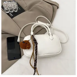 Close-up of white litchi pattern Boston bag with teddy bear charm and woven cord detail