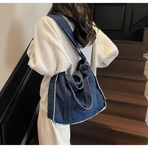 Deep blue denim tote bag with frayed edges worn by a model on a wooden staircase