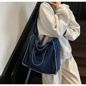 Detail of a large dark blue denim tote bag with frayed edges worn by a model