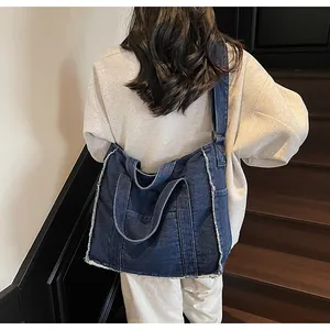Detail of blue denim tote bag with frayed edges worn by a model on a shoulder