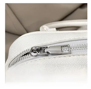 Macro shot of a silver metal zipper on white litchi pattern leather bag with fine texture