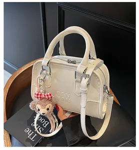 Close-up of cream glossy patent leather mini bag with embossed letters and bear charm