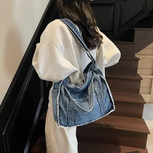 Fashionable denim tote bag with frayed edges and washed finish, shown crossbody on model