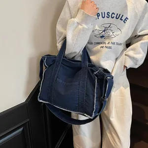 Large denim tote bag with frayed edges shown crossbody on model in a casual setting
