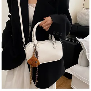 Detail of white lychee textured Boston bag with silver rings and plush bear charm