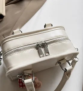 Close-up of smooth dual silver zippers and leather texture on a white crossbody bag