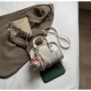 Detail of a creamy white Boston bag with embossed letters and a cute plush bear charm