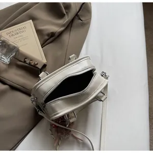 Detailed view of cream-colored Boston bag on bed with plush charm and leather strap