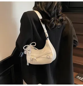 Close-up of cream hobo bag with pearl bow charm and lace fringe on stylish shoulder strap