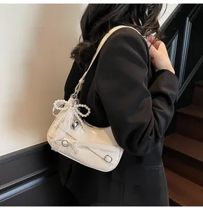Detail of cream hobo bag featuring pearl bow, lace ribbons and silver heart charm