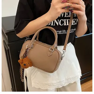 Close-up of khaki Boston bag with bear charm showing leather texture and style