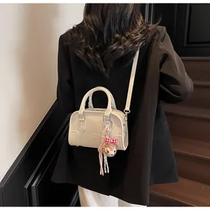 Detail of cream white embossed square bag with plush bear charm worn over the shoulder