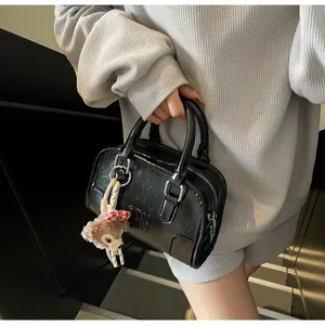 Detail of black Boston bag with textured leather, silver zipper, and plush bear charm