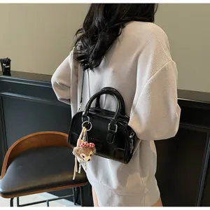 Detail view of black Boston bag with leather texture and plush bear charm on model