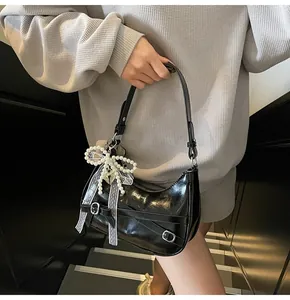 Close-up of black glossy crescent bag with lace bow and pearl charm pendant detail