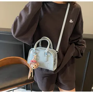 Detail of light blue crossbody bag with embossed letters and plush bear charm accent
